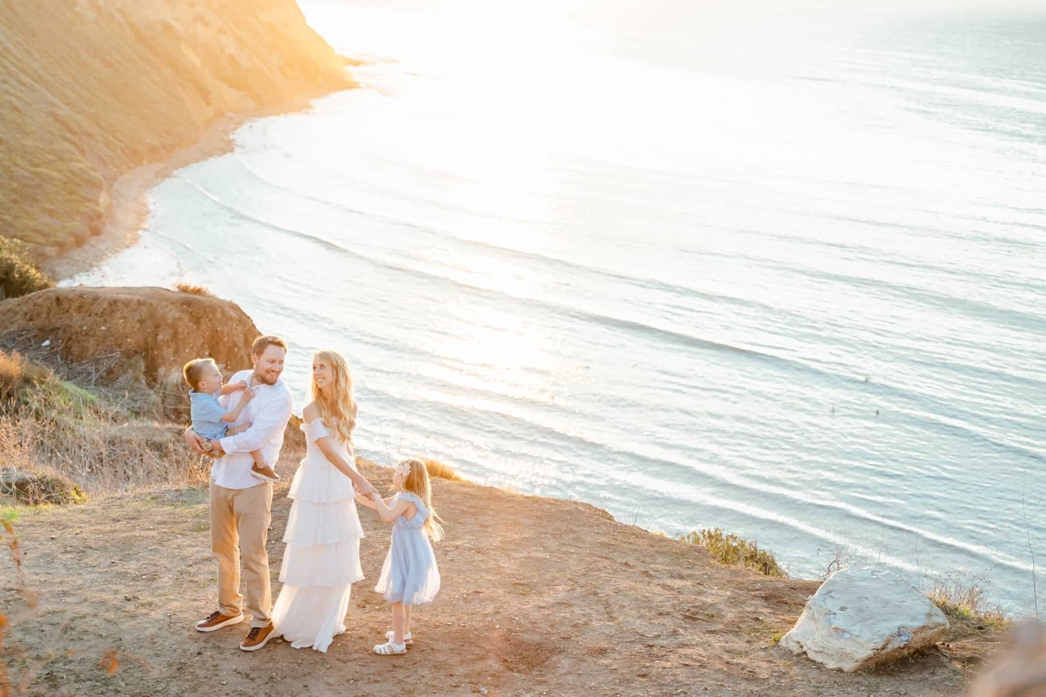 Family of four on California Cliffside dancing. Mom dancing with daughter, dad holding son, with parents looking at each other. Balboa Fun Zone