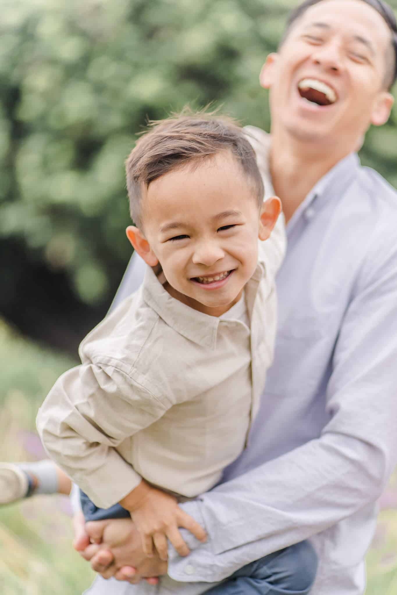 Son smiling at camera while dad is laughing in the background