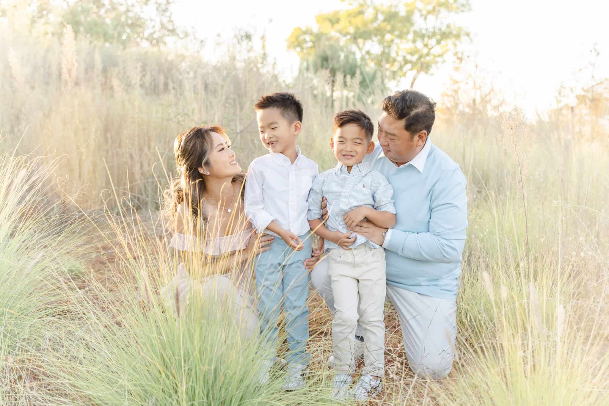 Asian family hugging in a field of tall grass with two boys right in the middle.