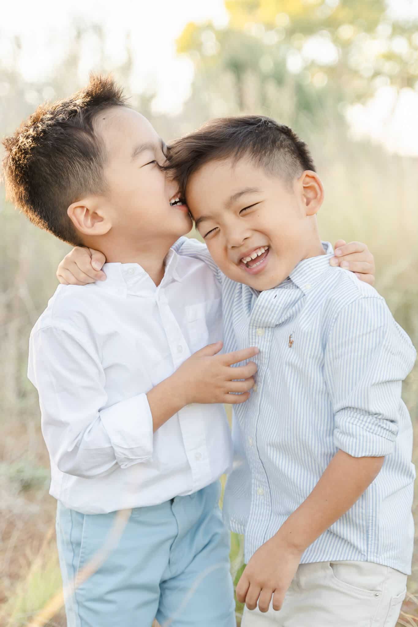 Two twin boys hugging each other with one kissing the other on the side of the head.
