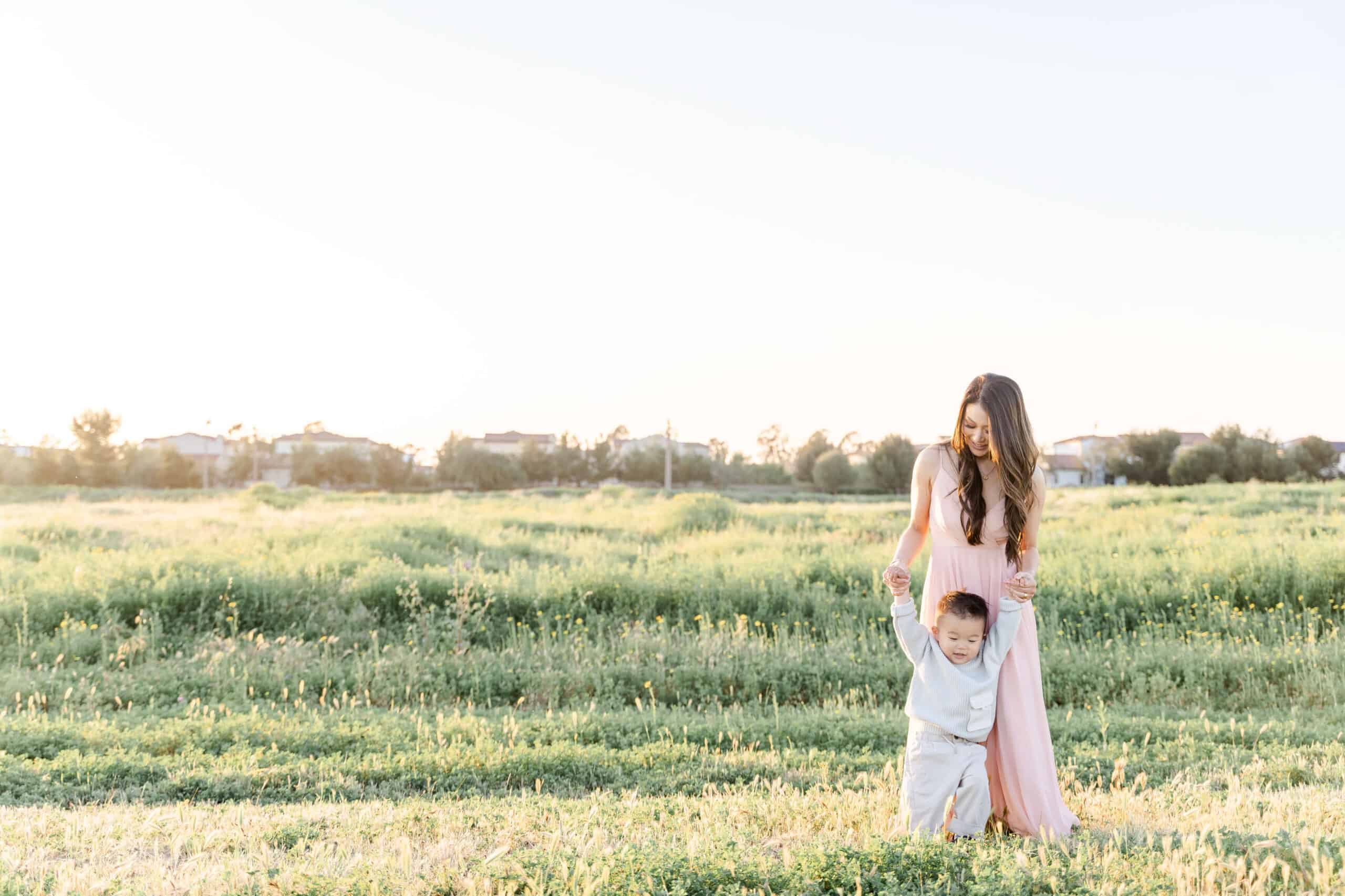 Mom holding toddler up by his hands in a field- Orange and Magnolia Dental Studio
