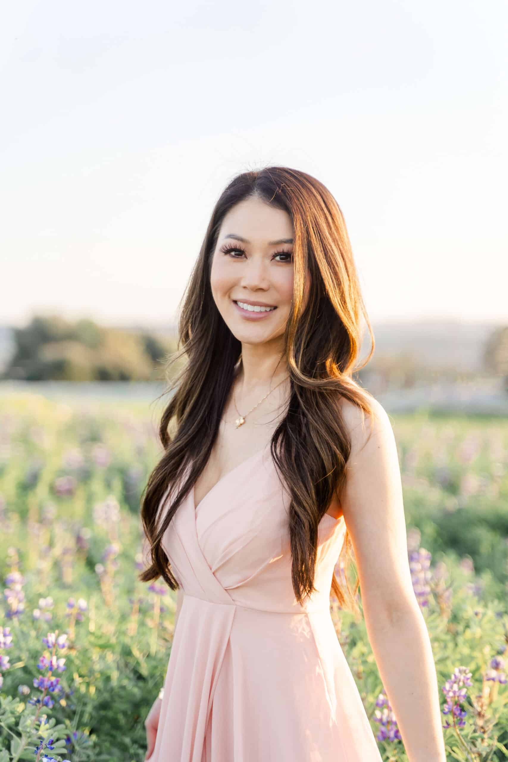 Young asian woman in pink dress standing in a field of flowers. Dr. Joyce Kahng of Orange and Magnolia Dental Studio