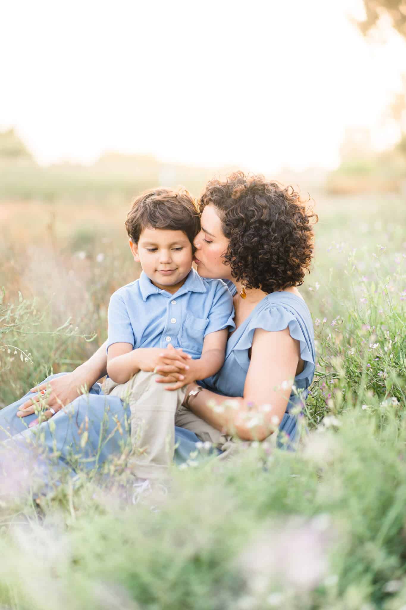 Mom kissing son in a field of grass