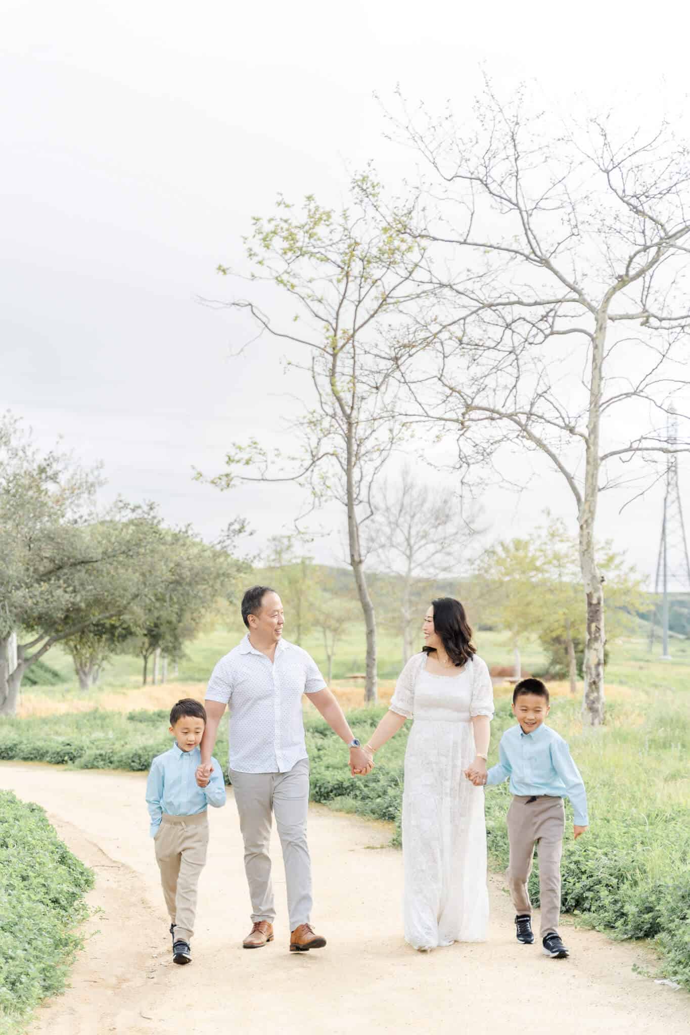 Mom and dad with two sons holding hands and walking down a dirt path in a grass field