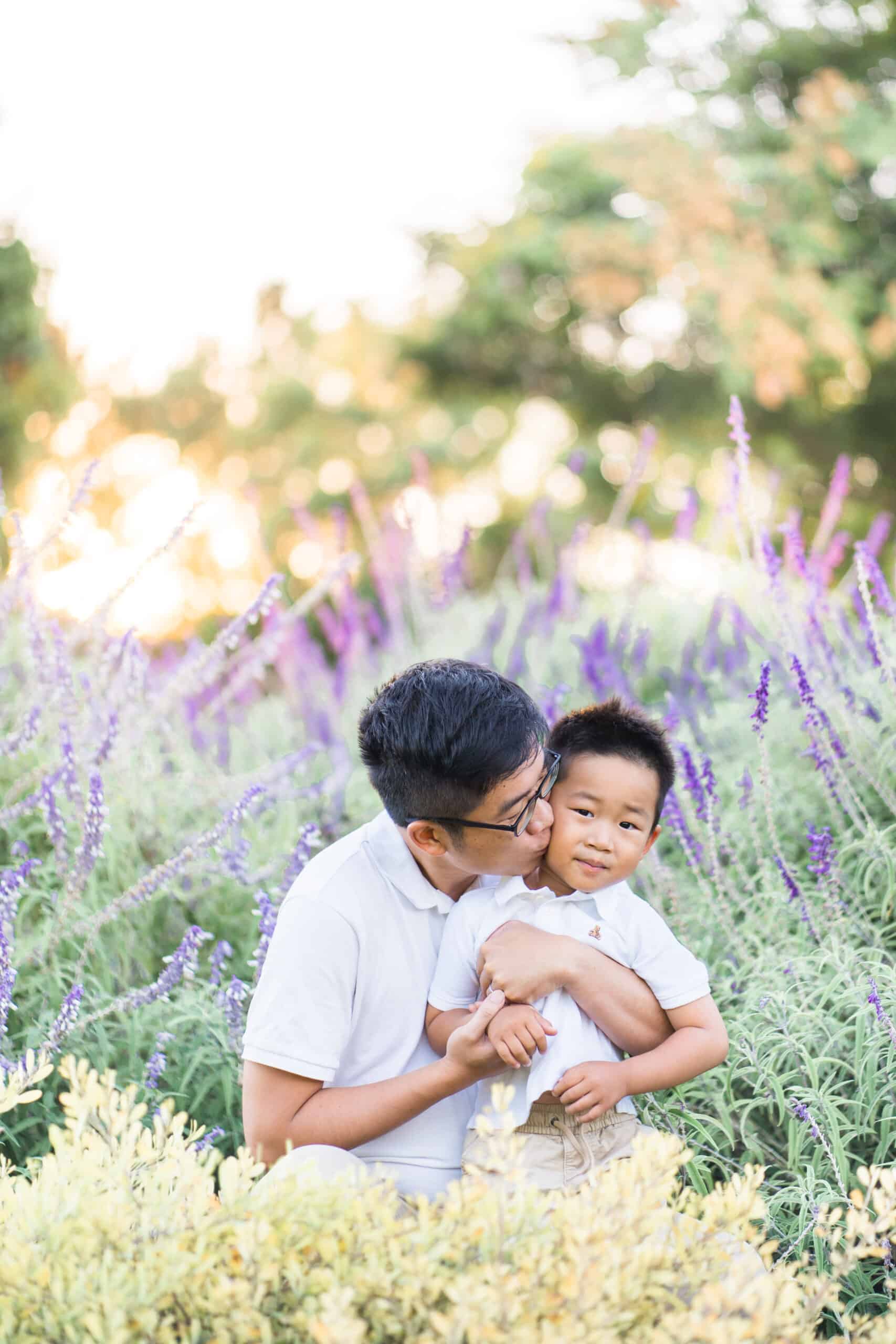 Dad with glasses kissing his son on the cheek in front of the lavender field. Blue Buoy Swim School