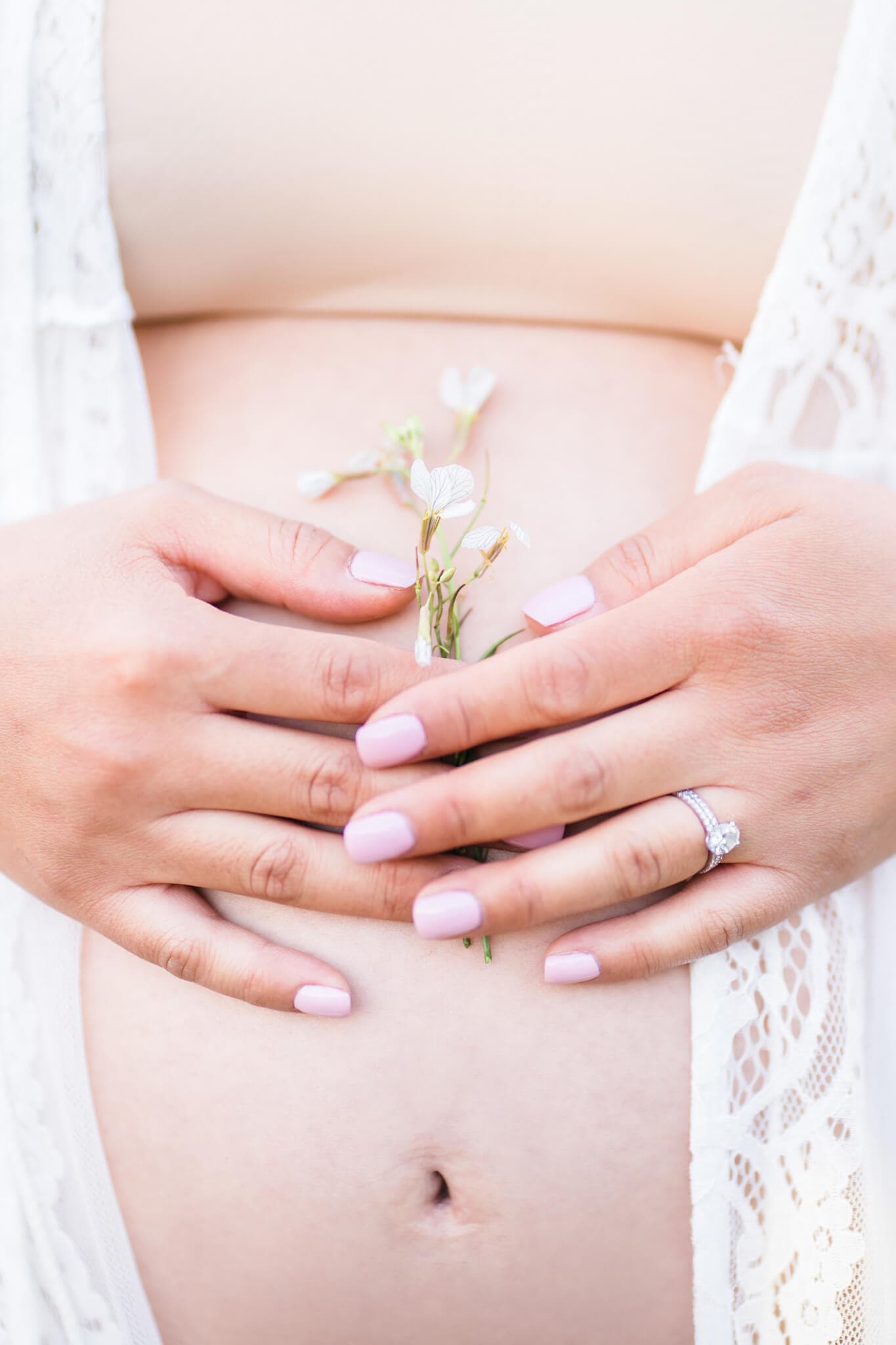 Mom holding white flowers to her bare belly. 