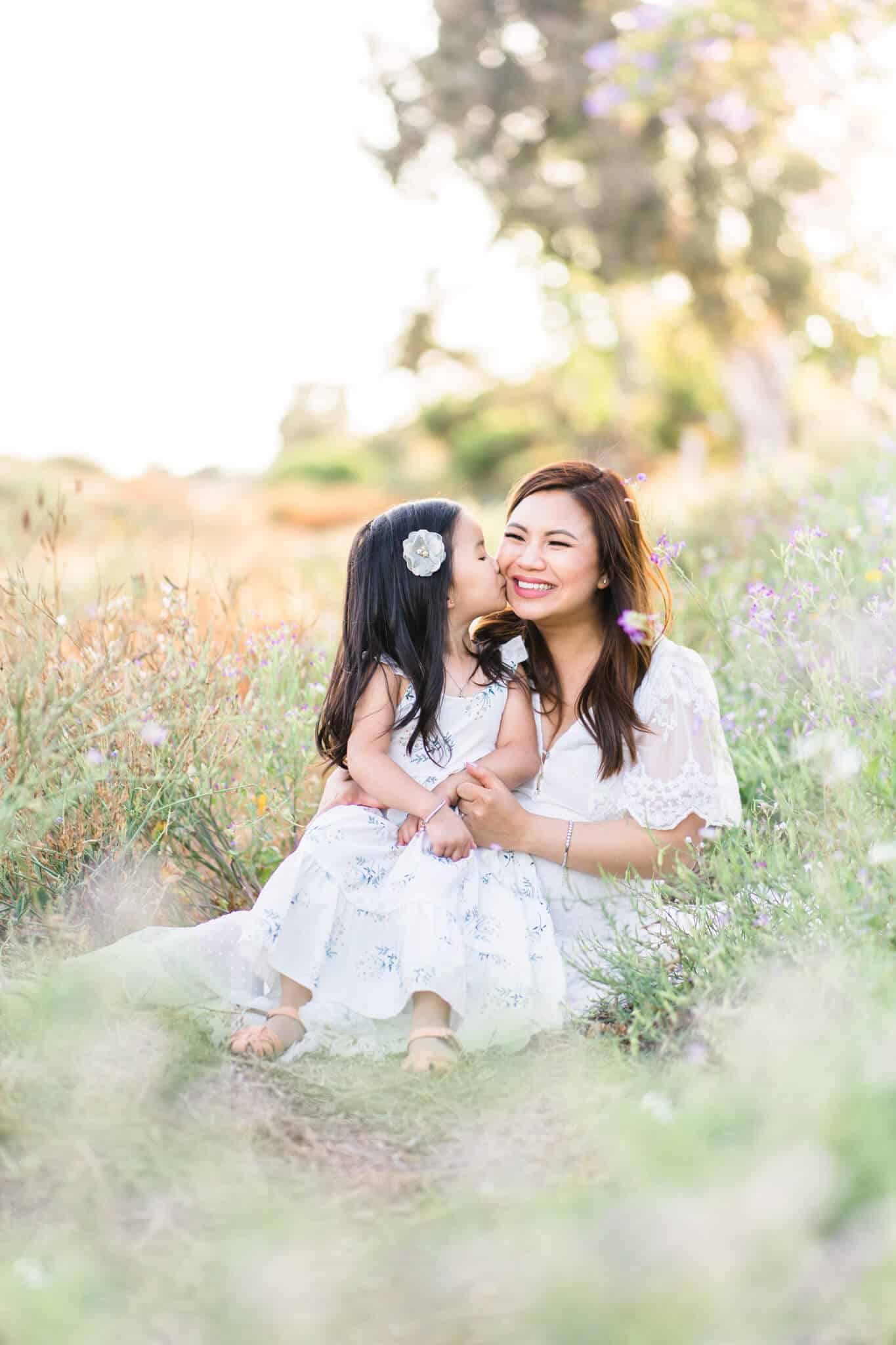 Mom and daughter sitting in a flower field with daughter kissing mom on the cheek. Orange Coast Women's Medical Group