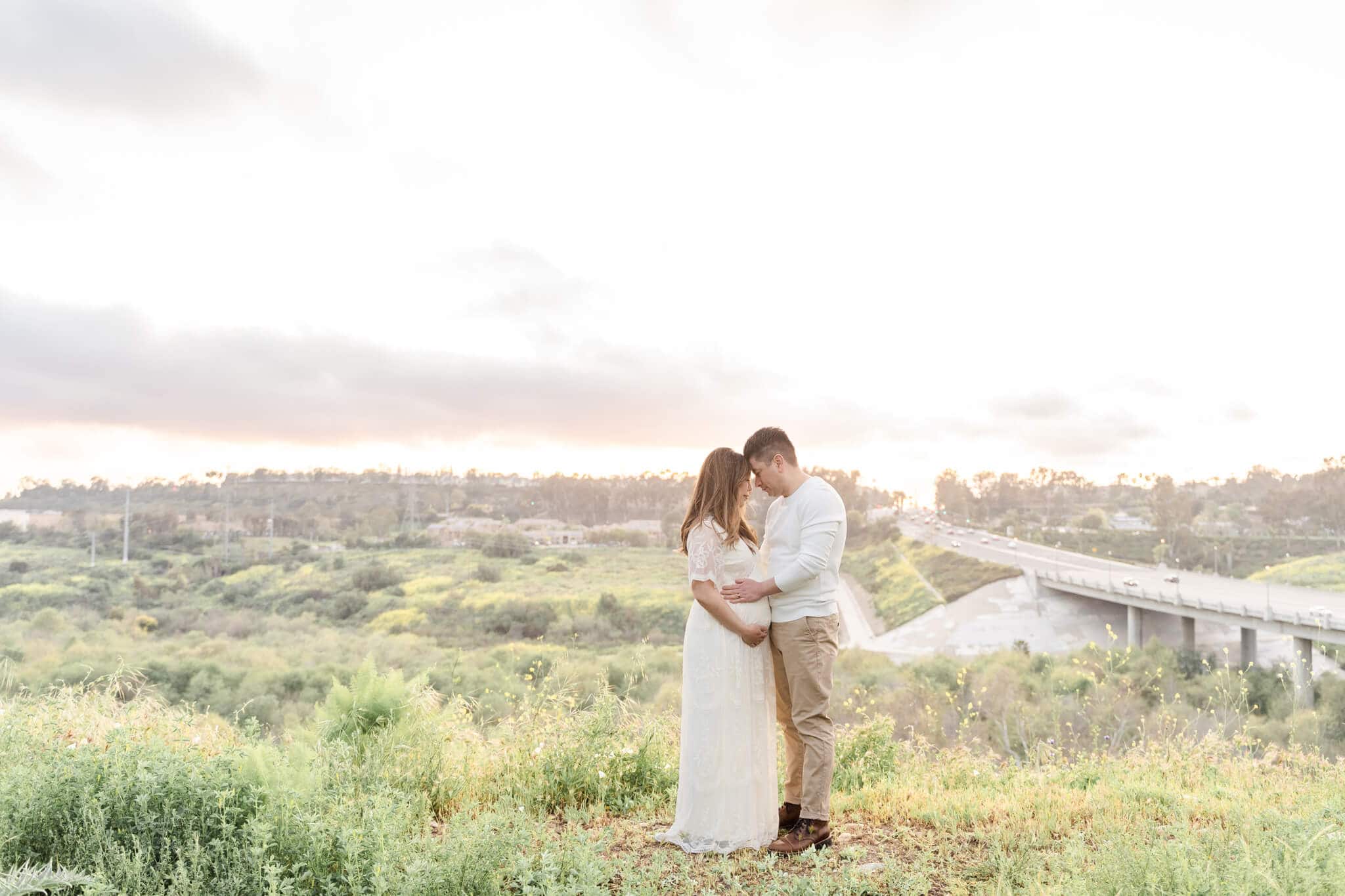 Pregnant couple standing foreheads touching on a hill around sunset. Newport Beach OBGYN