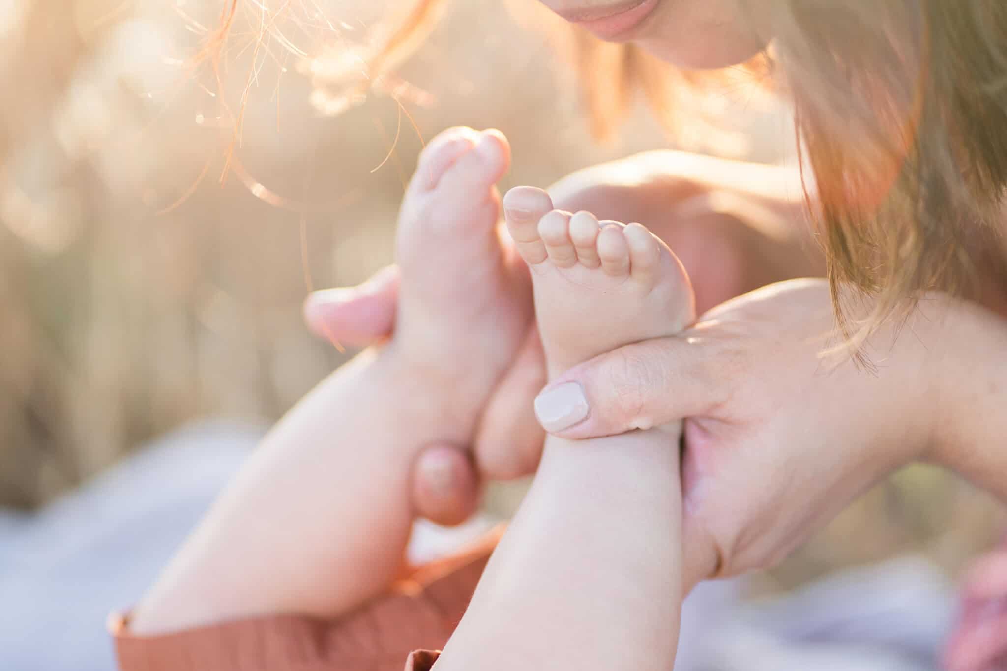 little baby toes and mom holding the feet on a picnic in a golden field