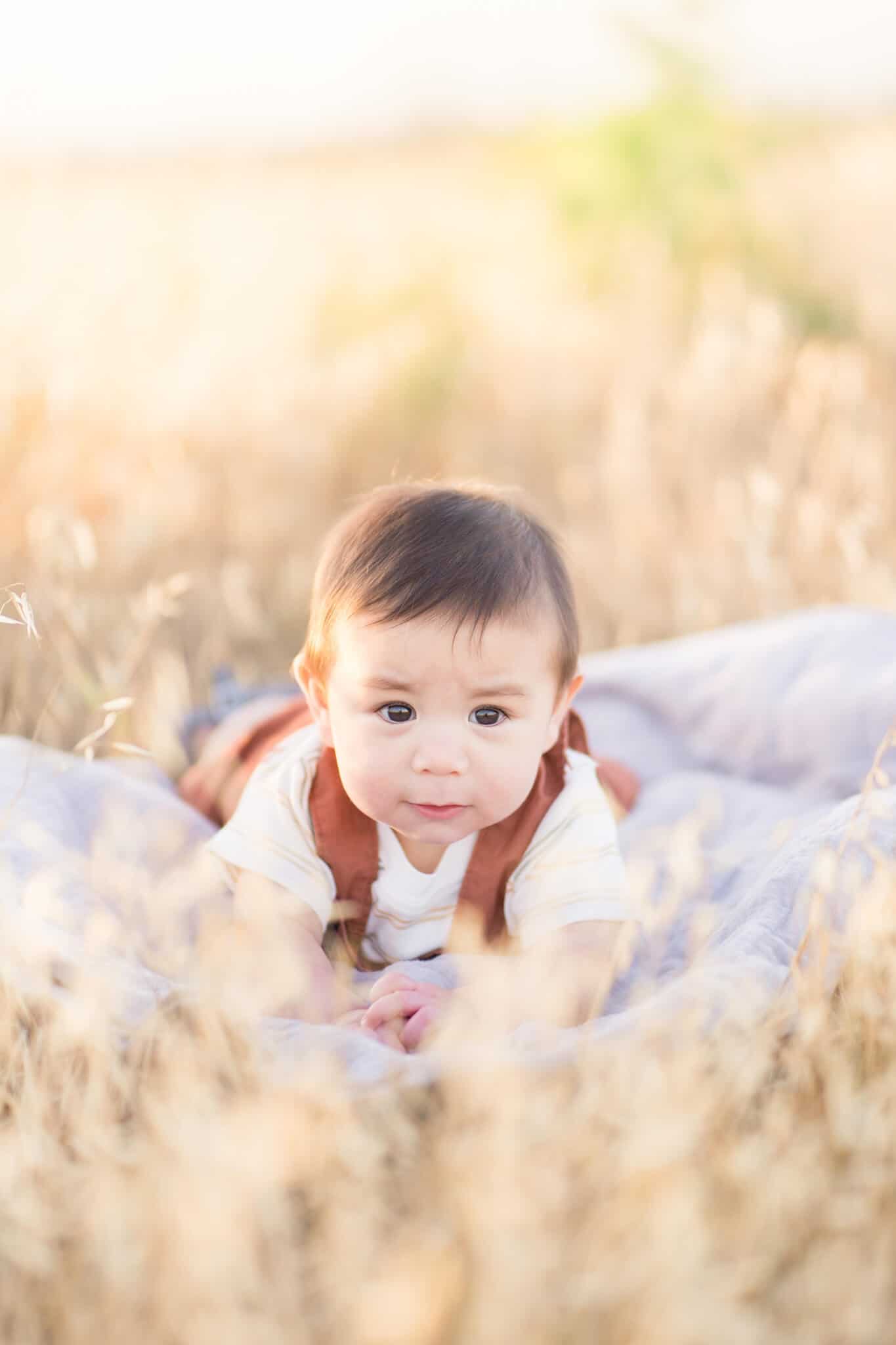 Little 9 month old boy in brown overalls doing tummy time on a beige blanket on a dry grass field- Irvine Pumpkin Patch