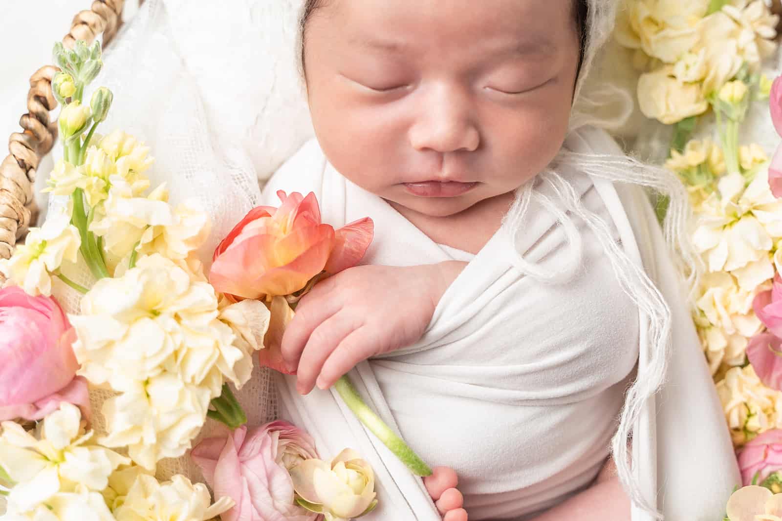 A newborn baby sleeps on a bed of flowers in a white swaddle after using OBGYN Lake Forest