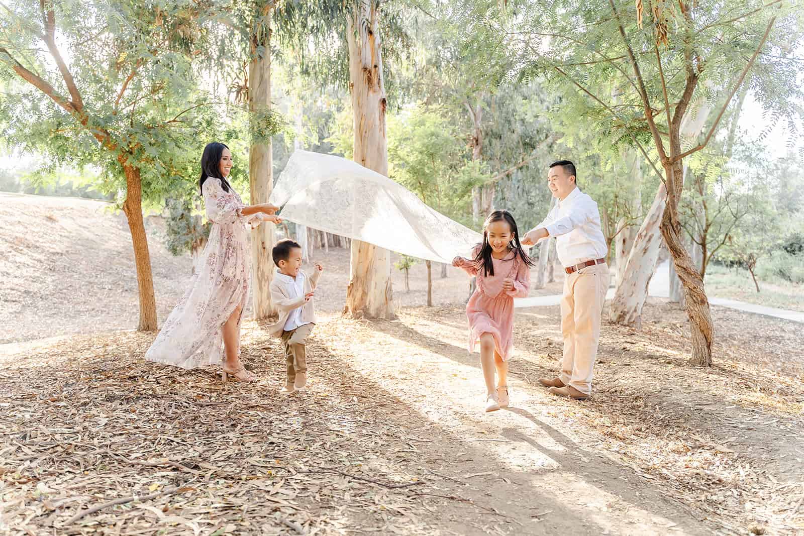 A mom and dad set out a picnic blanket while their daughter and toddler son run under it before a visit to Irvine Regional Park