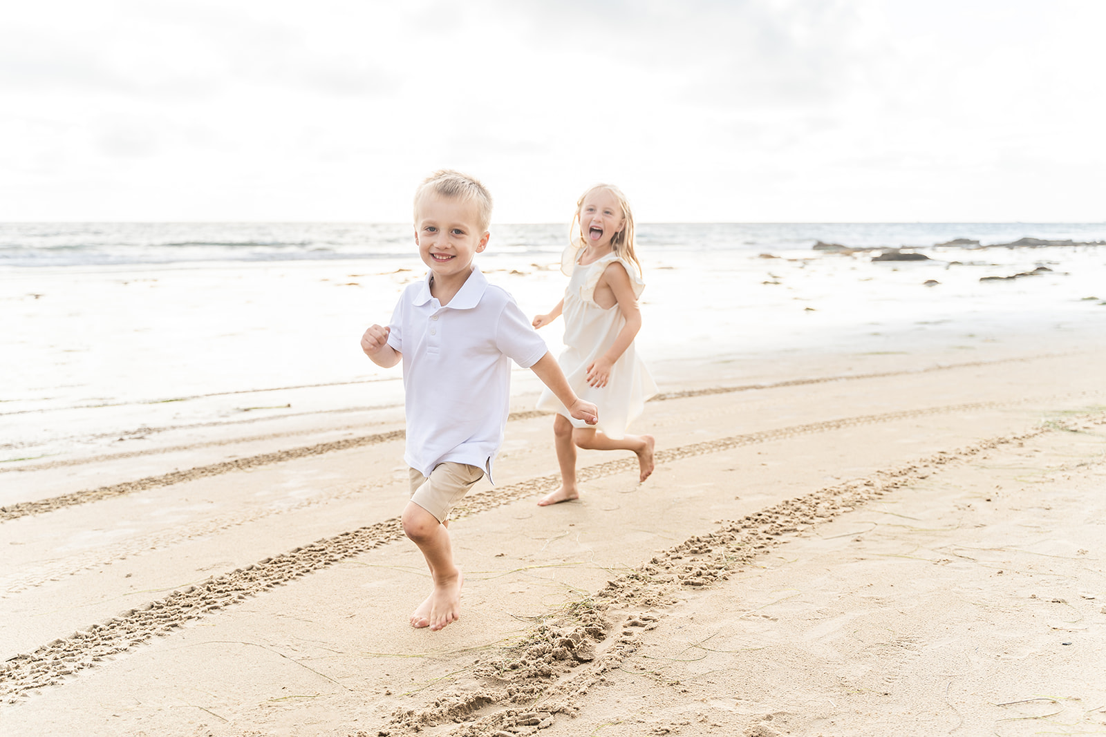 A young brother and sister run together on a beach