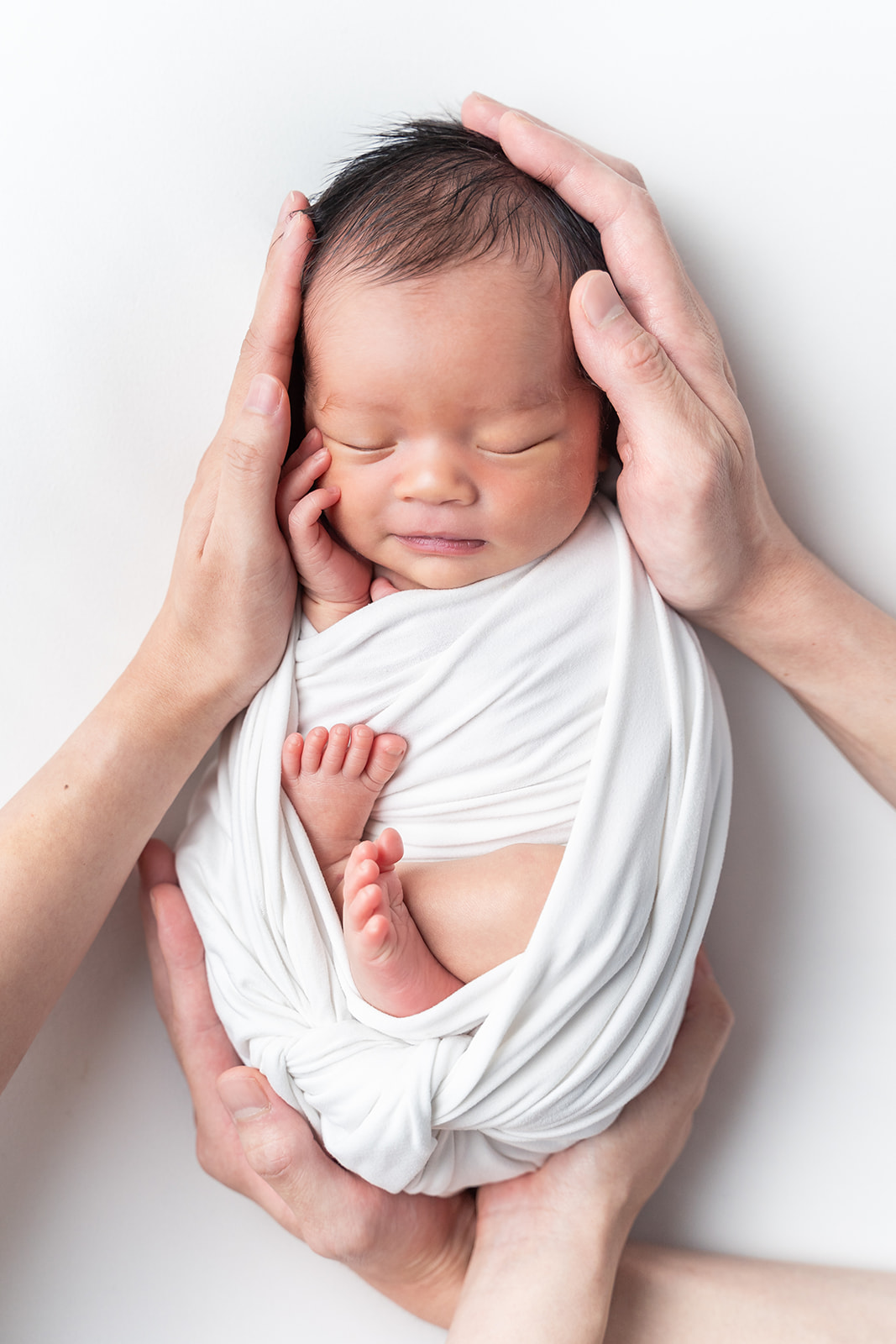 A newborn baby sleeps in a white swaddle while being cradled by parent's hands after using South Coast Midwifery