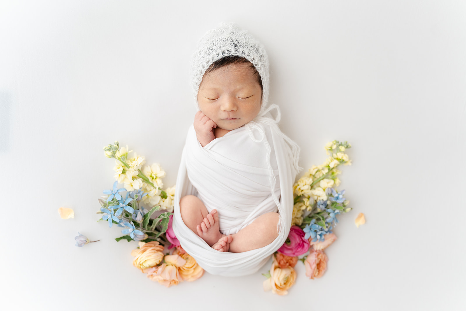 A newborn baby sleeps in a knit bonnet wirrounded by colorful flowers after using a Birthing Center Long Beach