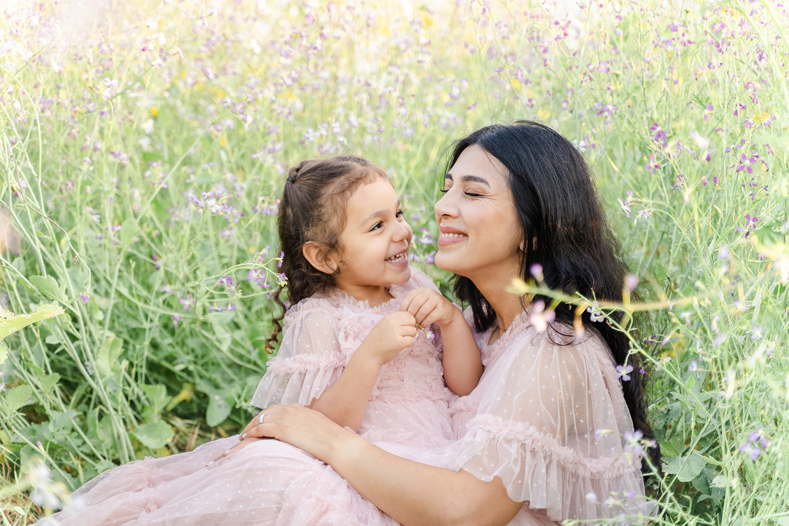 A mother in a pink dress sit in a field of wildflowers with her daughter in a matching dress after visiting Daycares in Irvine