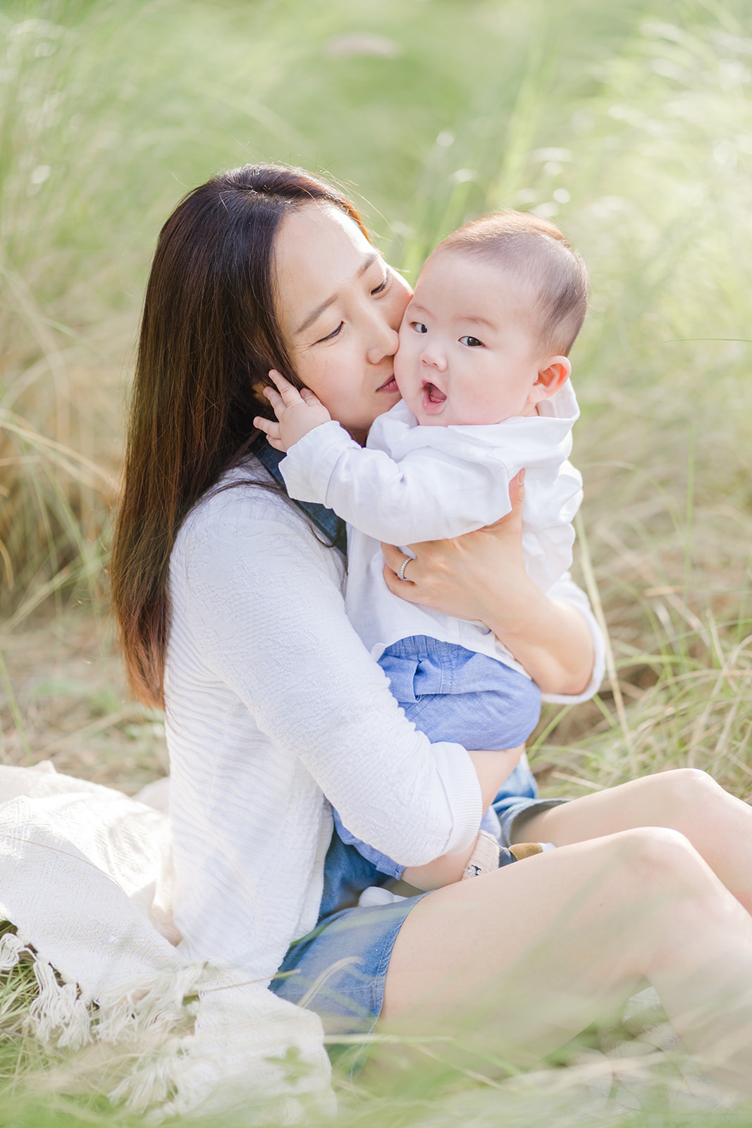 A mom kisses her infant son while sitting on a picnic blanket in a park before visiting Great Foundations Montessori Irvine