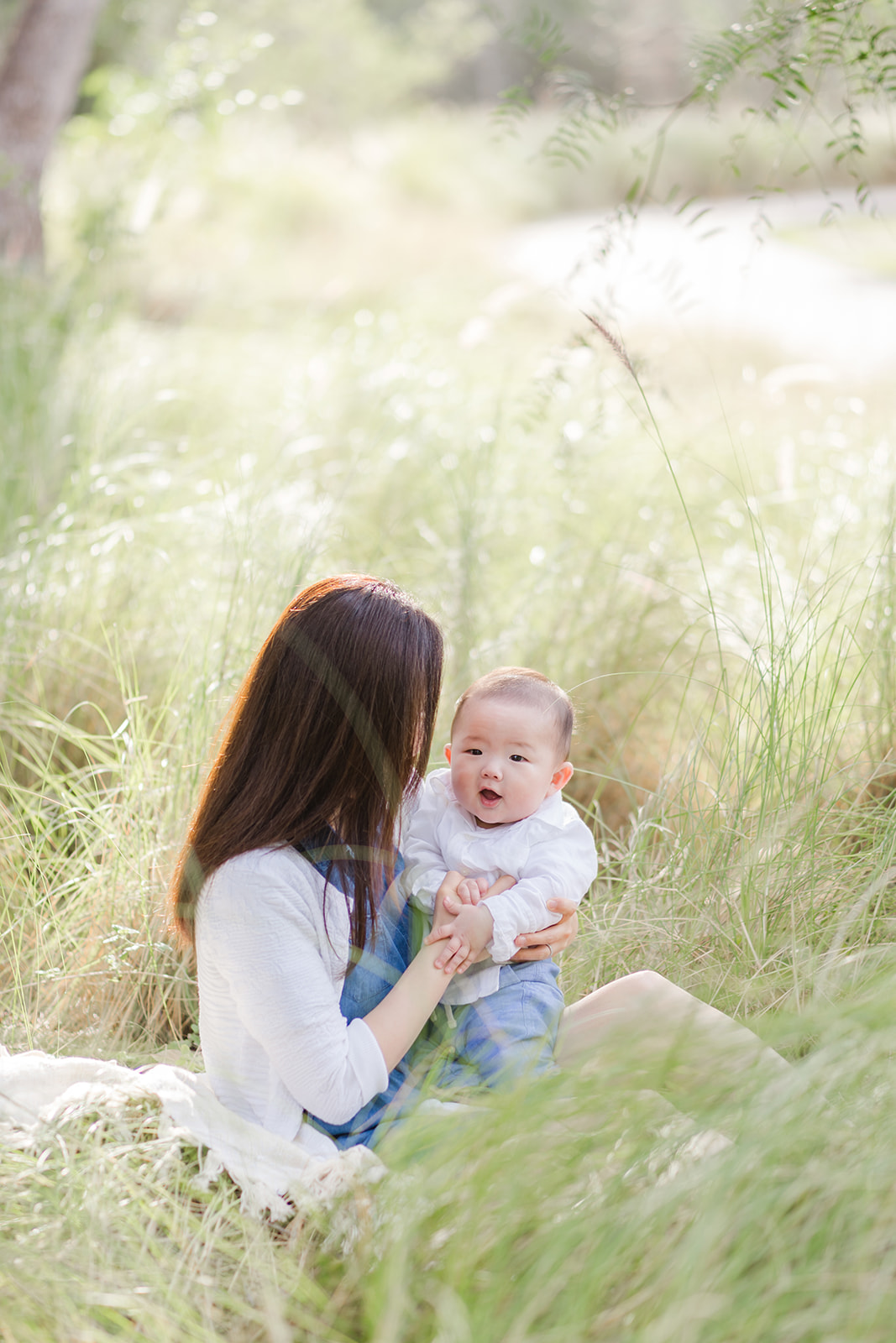 A mother sits in a field of tall grasses playing with her infant son at sunset before visiting Great Foundations Montessori Irvine