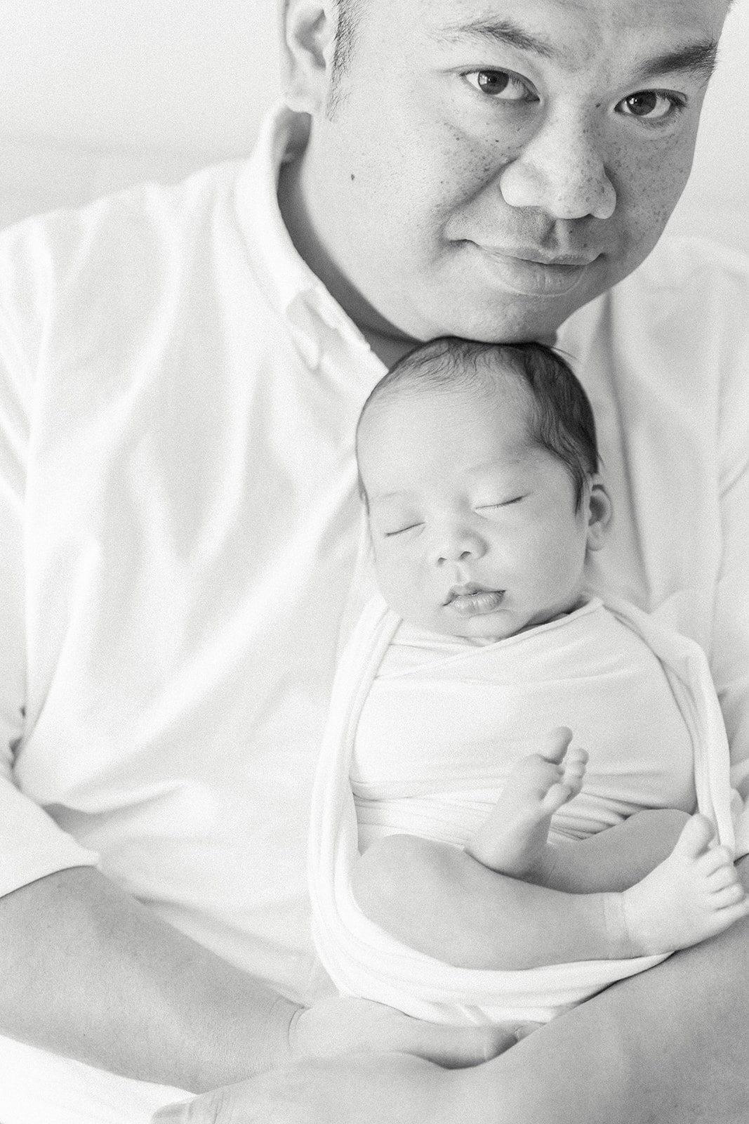 A happy dad stands in a studio with his newborn baby under his chin