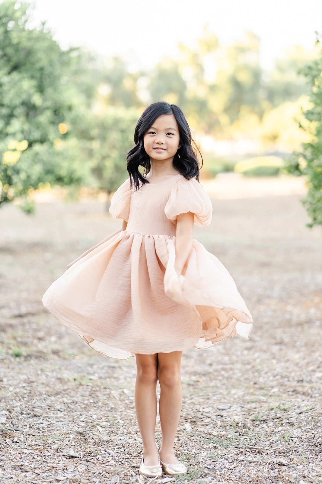 A young girl in a peach dress twirls while standing in an orange grove