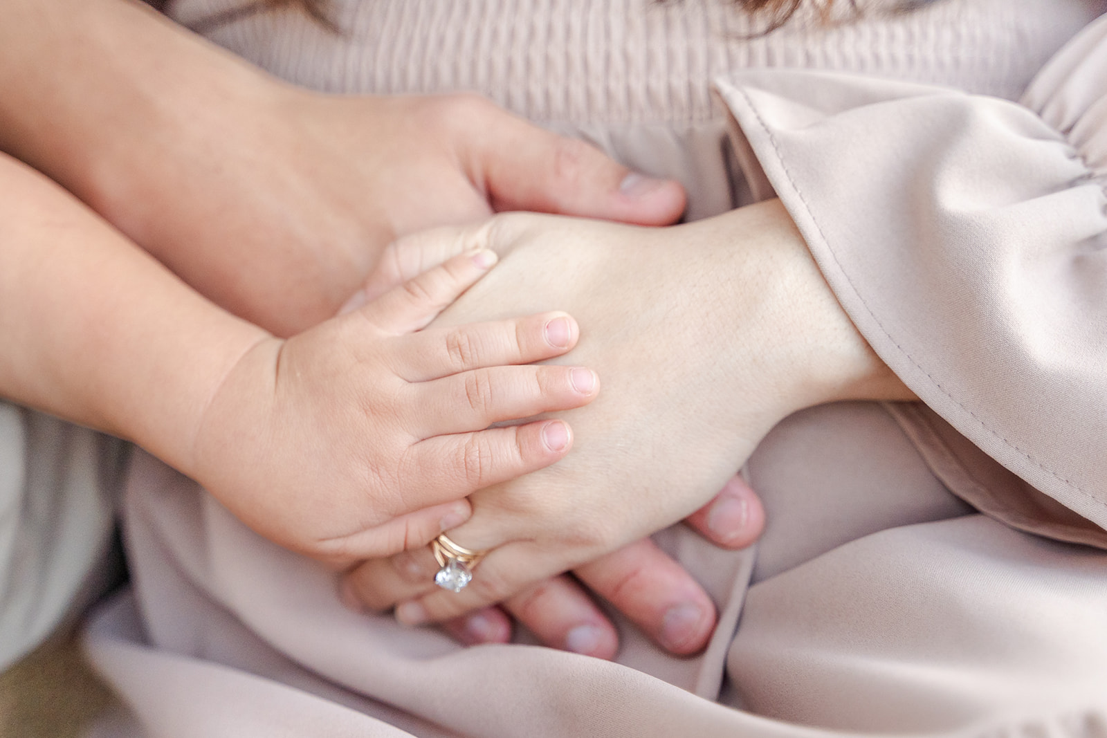 Details of a dad, mom and toddler placing hands on mom's pregnant bump