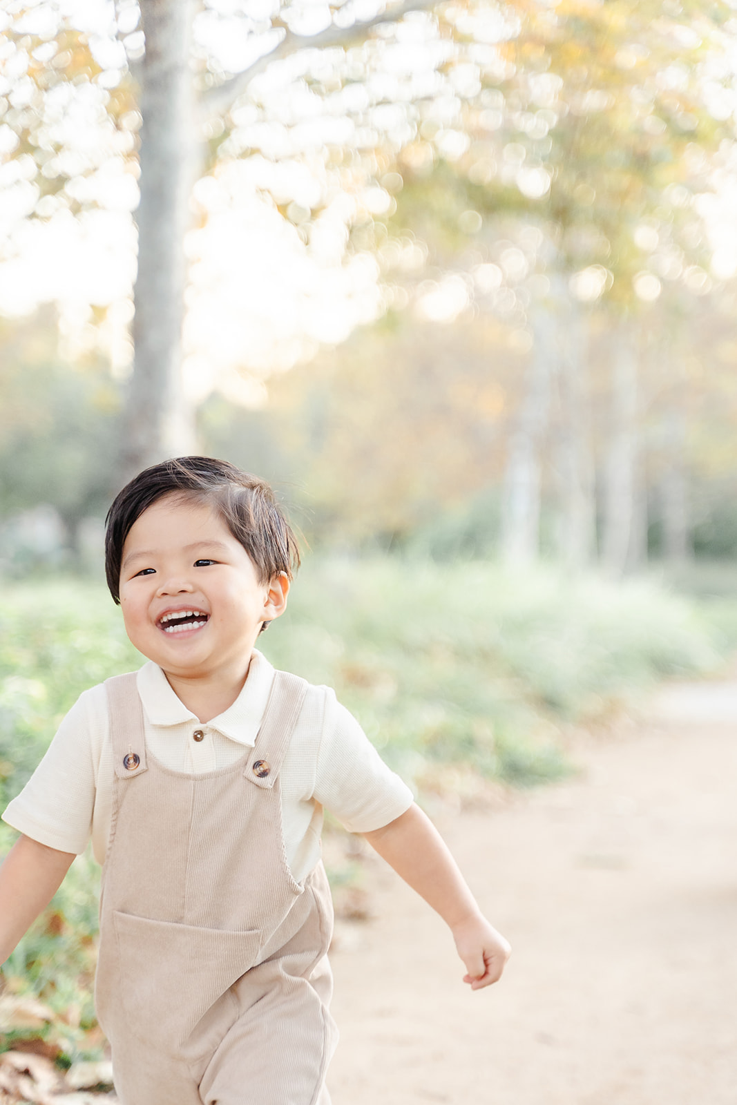 A young boy in tan overalls smiles while walking down a park path at sunset after attending Preschool in Irvine