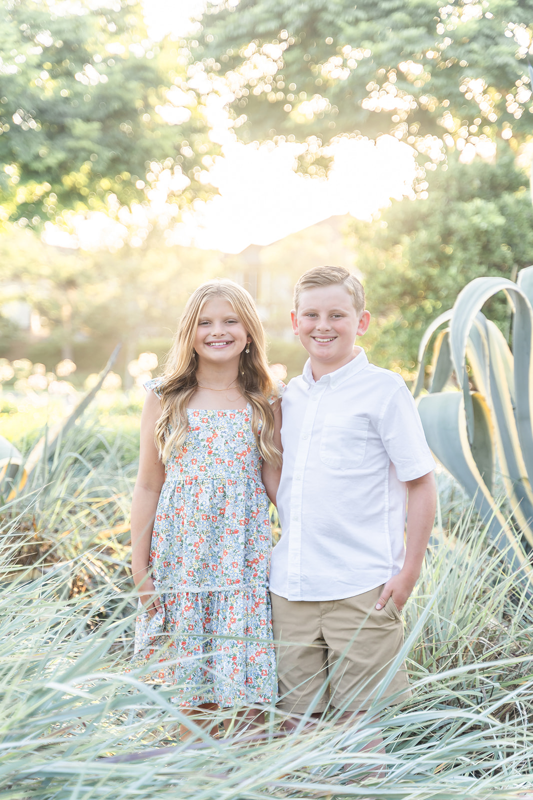 A young brother and sister stand together in a park garden at sunset