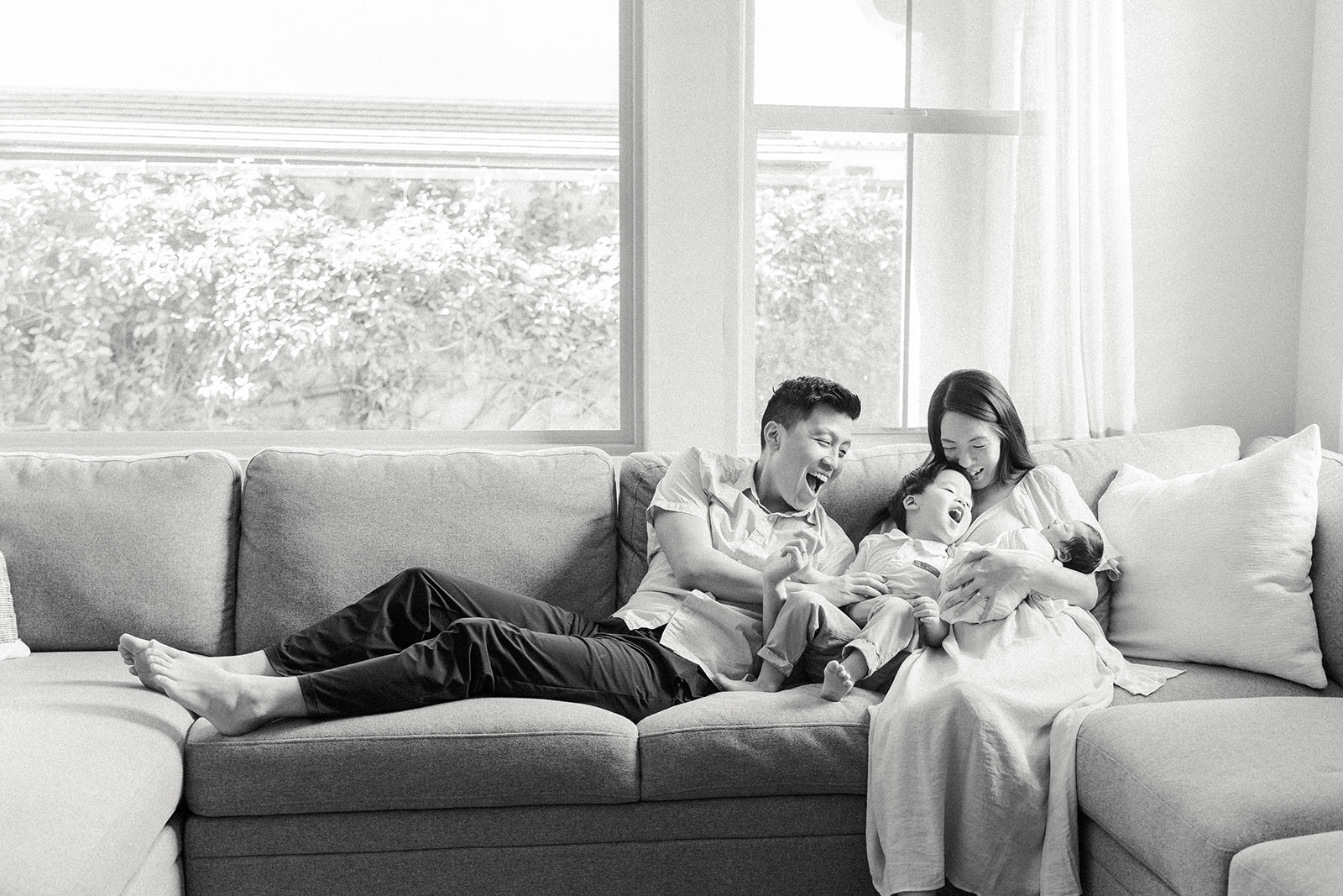 A mom and dad sit across a sofa playing with their toddler son and newborn baby after visiting Treehouse Pediatric Dentistry