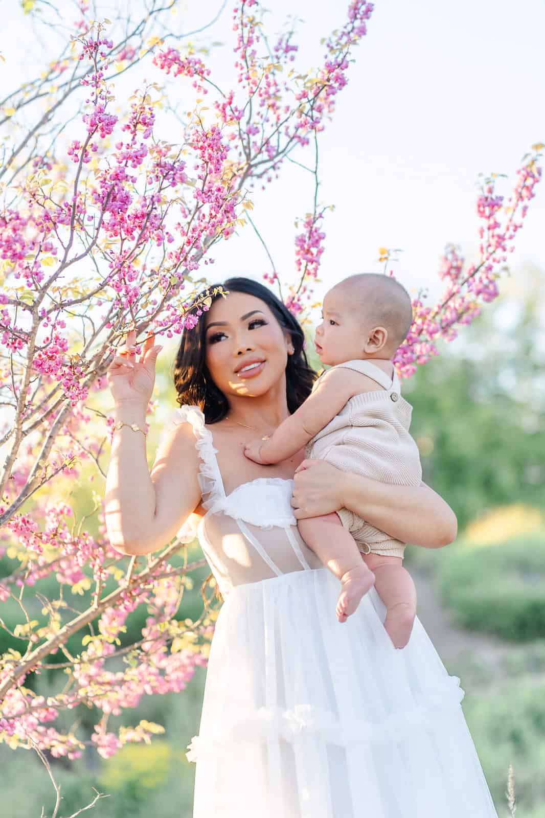 A mother shows a blossoming pink tree to her infant in her arms