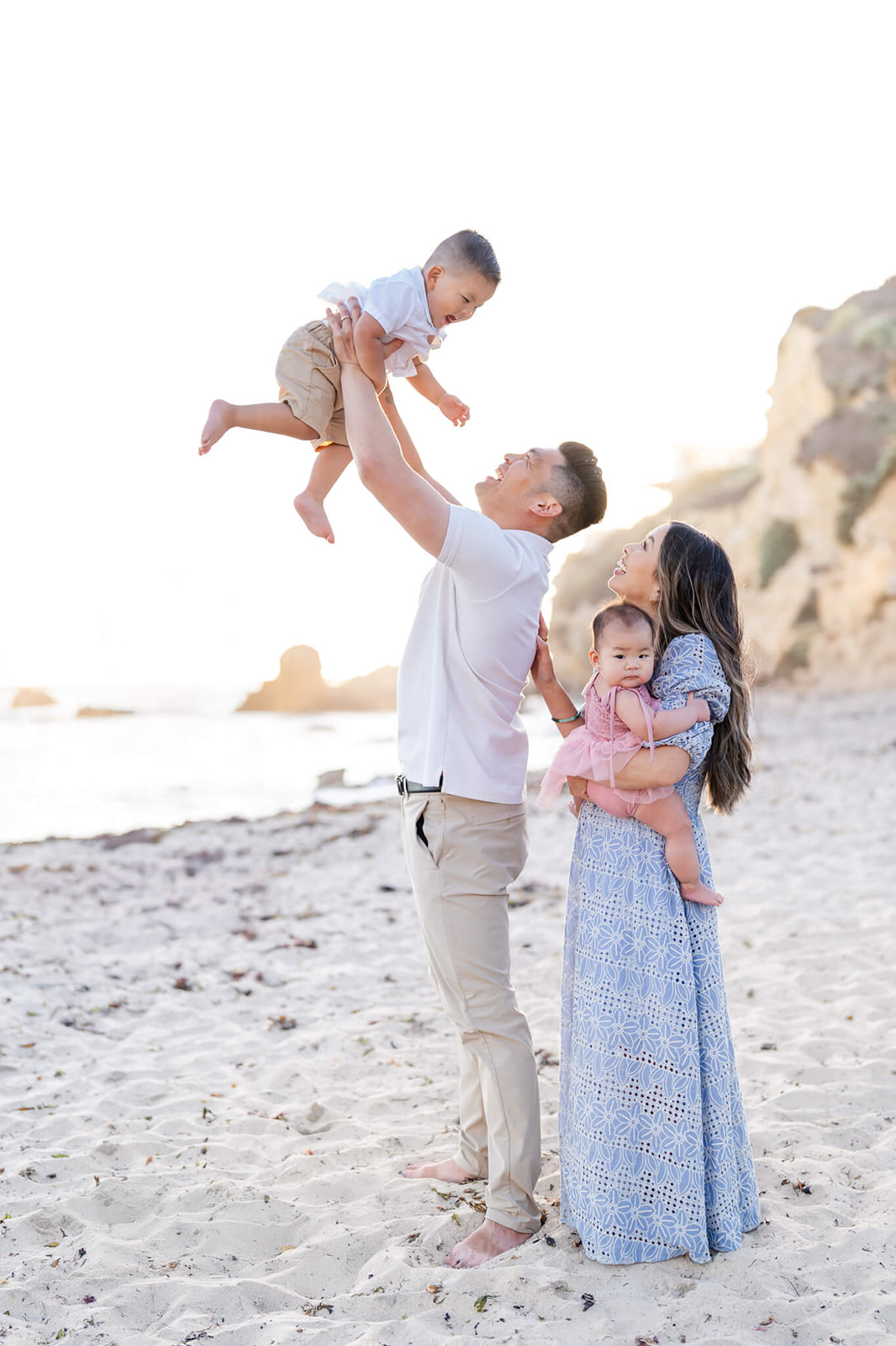 Happy mom and dad in blue and white laugh and play with their two toddlers on a beach
