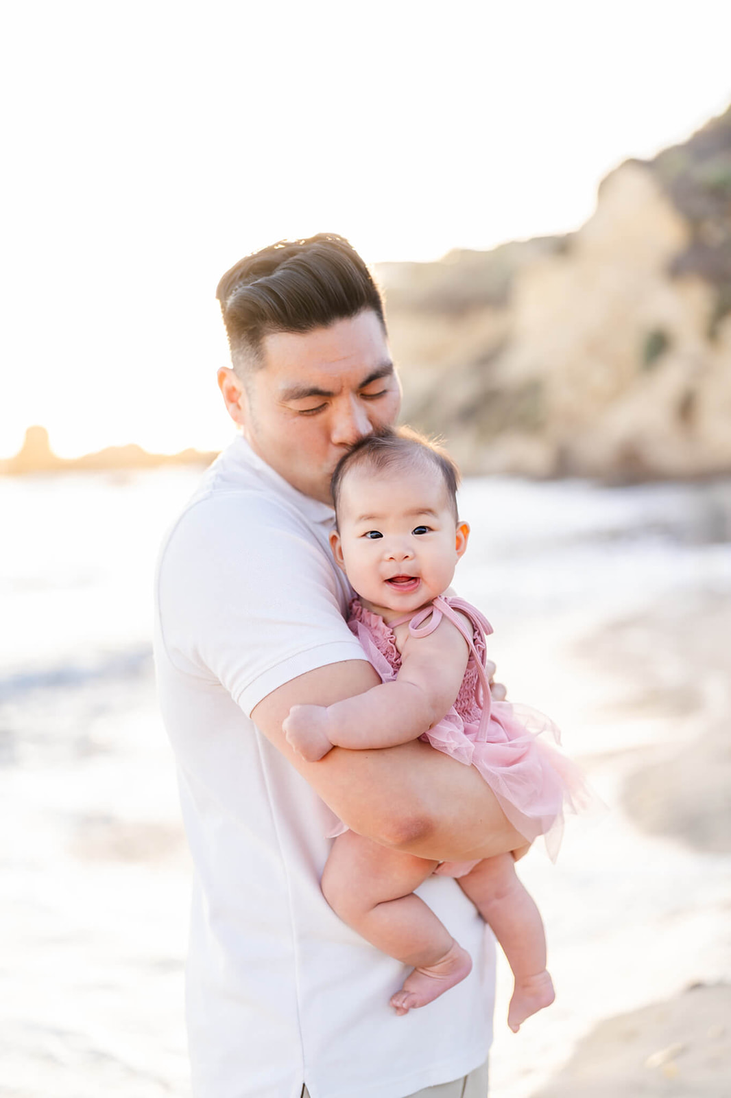 A happy baby girl is kissed by dad while being held on a beach at sunset before visiting Seascape Kids Fun