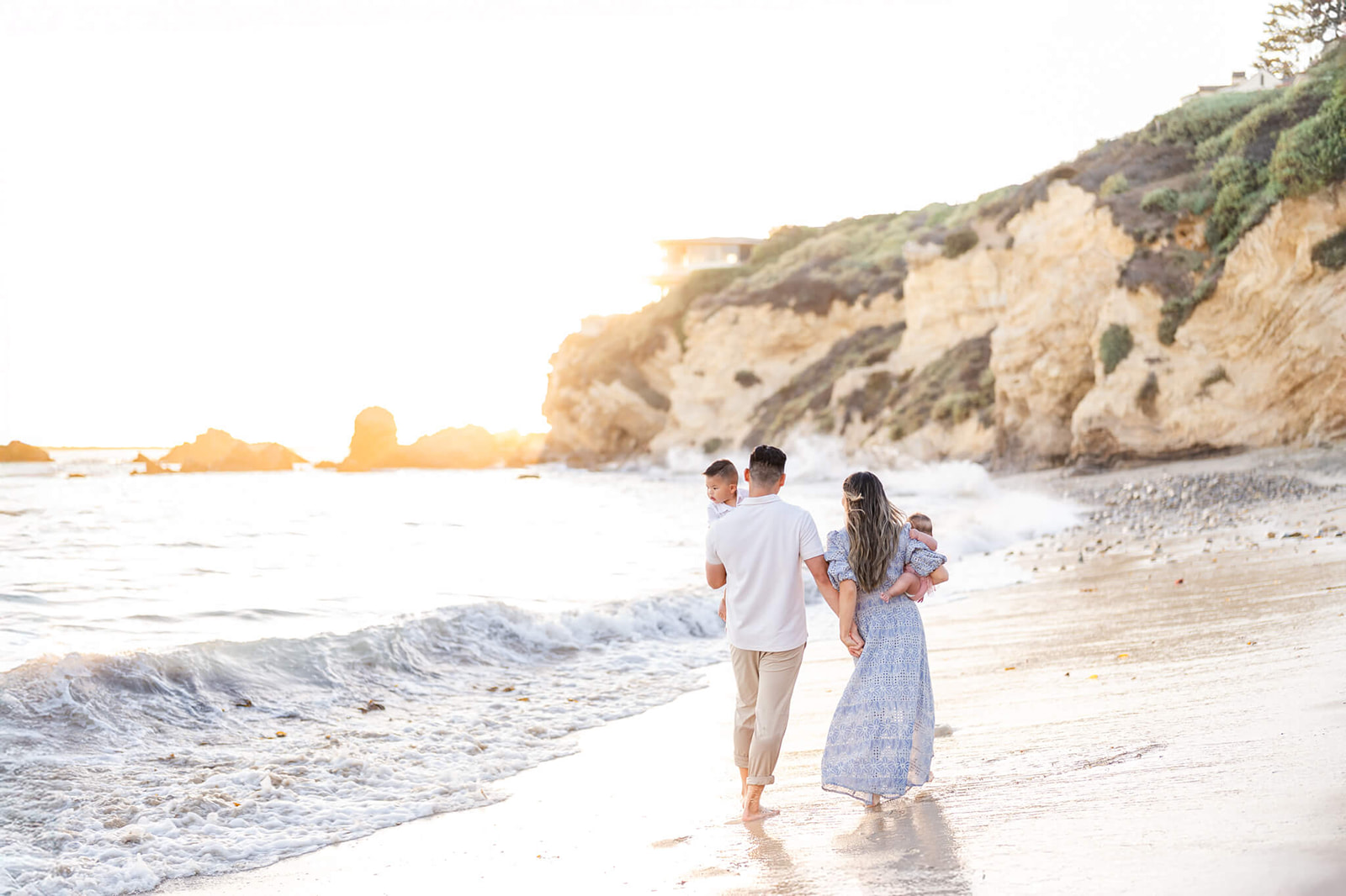 A mom and dad in white and blue walk on a beach holding hands and carrying their two toddlers at Seascape Kids Fun