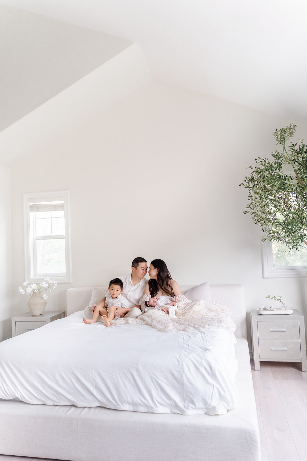 Mom and dad sitting on a bed with their newborn and toddler son in their laps after visiting Irvine Chinese Immersion Academy