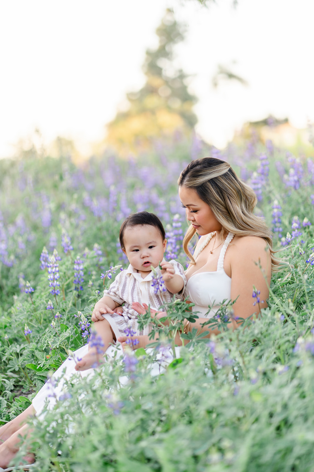A toddler sits in mom's lap picking purple wildflowers at sunset while visiting Irvine parks