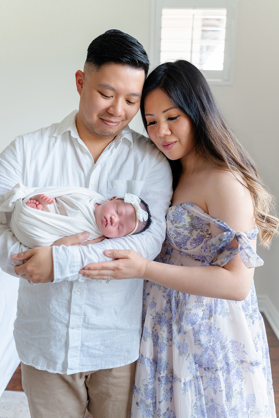 A newborn baby sleeps in a tight swaddle on her side in dad's arms as mom snuggles on dad in a blue dress after visiting Community Roots Academy