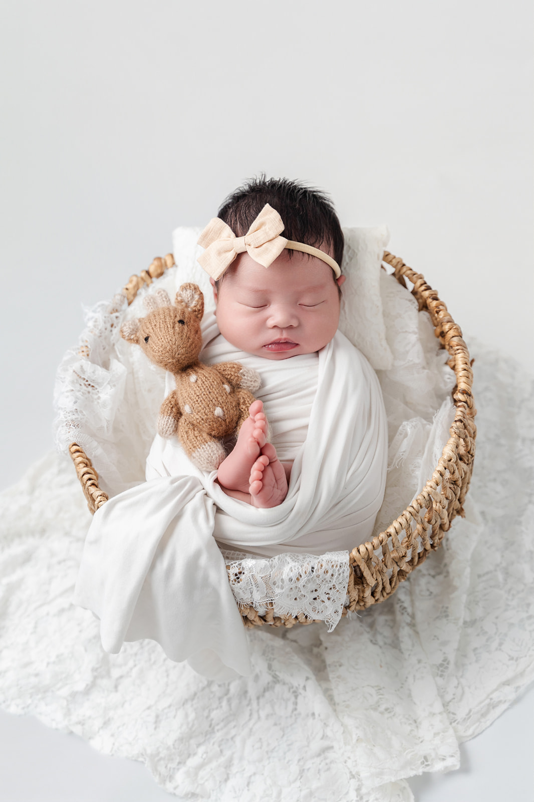 A newborn girl sleeps in a woven bowl in a white swaddle with a knit giraffe