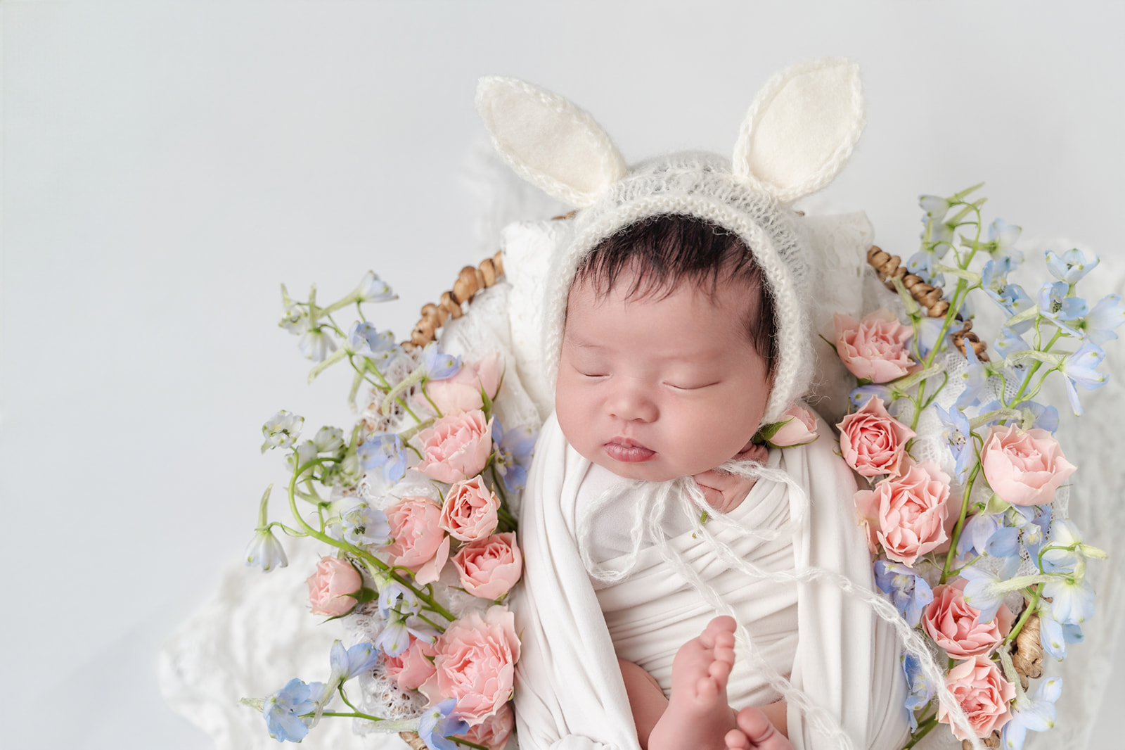 A baby girl in a flower basket wearing a knit white bunny ears bonnet