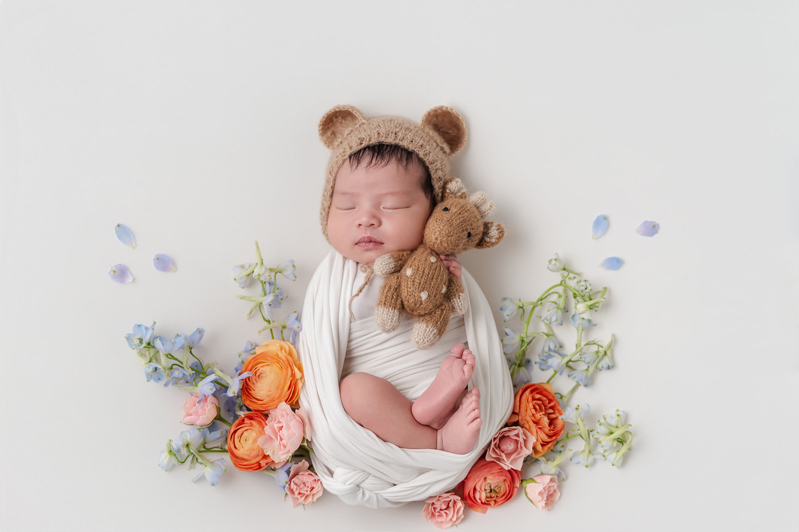 A newborn baby sleeps in a knit bear ear bonnet snuggling a knit giraffe while in a whtie swaddle after exploring Northwood Montessori School