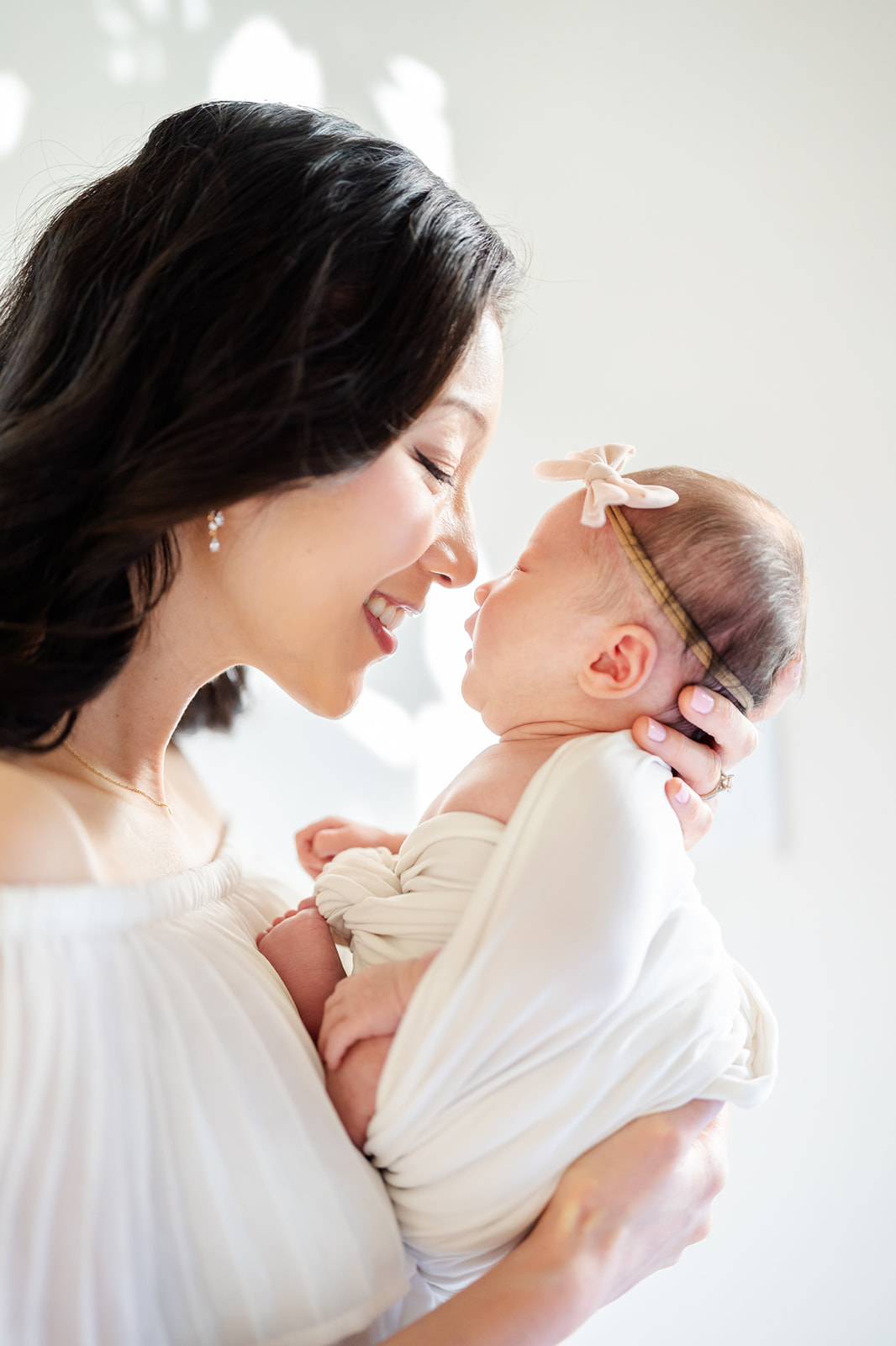 A happy mother in white boops noses with her newborn in her hands in a white swaddle before visiting The Rinks Irvine